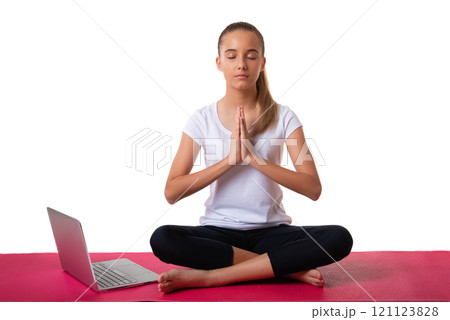 Inner power. Young woman sitting in pose of lotus and putting her palms together on her chest area with laptop on yoga mat, isolated on white background Inner power. Young woman sitting in pose of lotus and putting her palms together on her chest area with laptop on yoga mat, isolated on white background 121123828