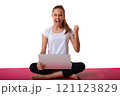 Emotional sporty young woman sitting in pink yoga mat in pose of lotus shout loud yeah fist up raise and using laptop , isolated on white background 121123829