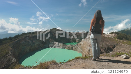 Tourist woman enjoy morning view on volcanic Kelimutu blue crater lakes. Nature background. Travel destination. Beautiful wild landscape. Exotic summer vacation, hiking, relax. Close up back view 121124970