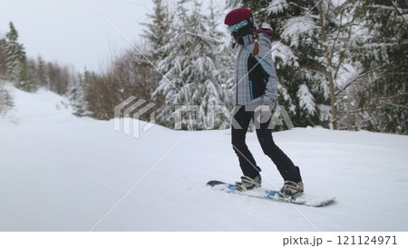 Woman learning snowboard riding on snowy slopes of ski resort. First time beginner. Winter vacation, active sport lifestyle. Bukovel mountains, Ukraine. Slow motion 121124971