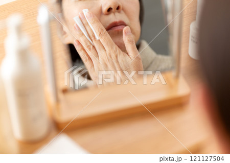 鏡の前で基礎化粧品を使ってスキンケアするミドル〜シニア女性 鏡の前で基礎化粧品を使ってスキンケアするミドル〜シニア女性 121127504