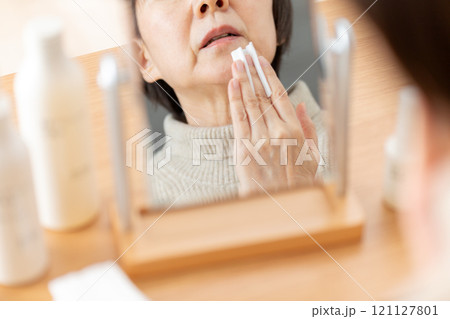 鏡の前で基礎化粧品を使ってスキンケアするミドル〜シニア女性 鏡の前で基礎化粧品を使ってスキンケアするミドル〜シニア女性 121127801