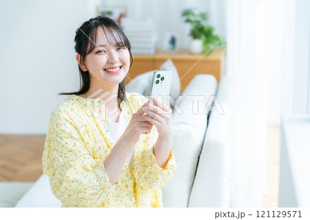 部屋でスマホを操作する若い女性 121129571