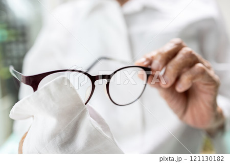 Hands of senior woman holding eyeglasses,elderly cleaning the lenses of glasses with her shirt,old grandmother using her clothes to wipe spectacles,wrong,incorrect cleaning of glasses,not correct 121130182