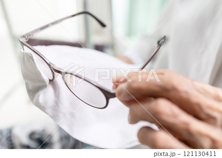 Close up of spectacles,hands of senior woman holding eyeglasses,old elderly cleaning the lenses of glasses with her shirt,using her clothes to wipe spectacles,cleans glasses from dust and dirt 121130411