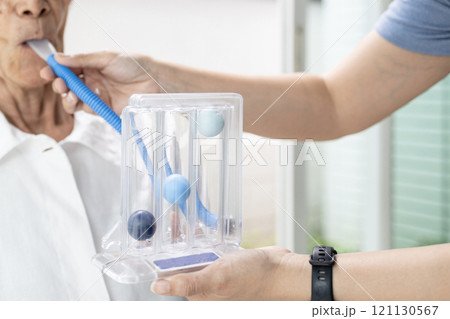 Asian female caregiver holding spirometer,taking care of senior grandmother at nursing home,elderly using spirometer,exercise the lung,help the lung expansion,concept of service,medical,health care 121130567