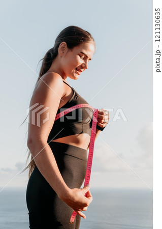 A woman is holding a pink tape measure and is measuring her breasts after morning fitness 121130635