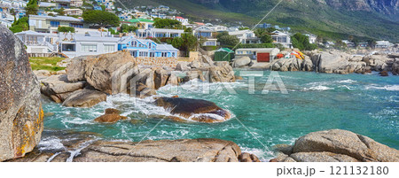 Scenic view of sea, rocks and residential buildings in Camps Bay Beach, Cape Town, South Africa. Tidal ocean waves washing over shoreline rocks and boulders. Overseas travel and tourism destination 121132180