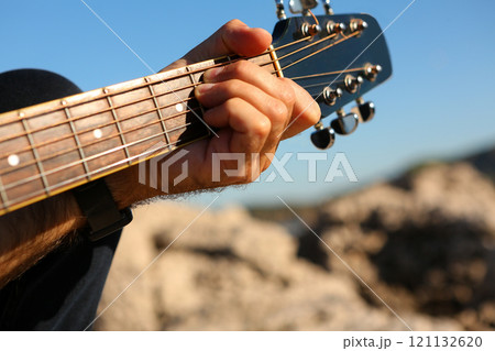 Close-up of a man playing the E chord on an acoustic guitar 121132620