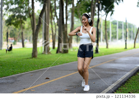 Sporty young woman checking her fitness progress on her smartwatch while jogging in a park Sporty young woman checking her fitness progress on her smartwatch while jogging in a park 121134336