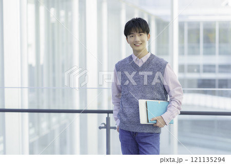 ノートパソコンと手帳を持って立つ若い男性のポートレート ノートパソコンと手帳を持って立つ若い男性のポートレート 121135294