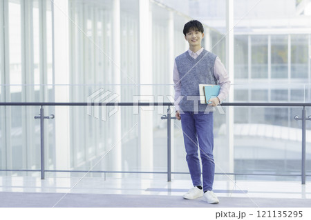 ノートパソコンと手帳を持って立つ若い男性のポートレート 121135295