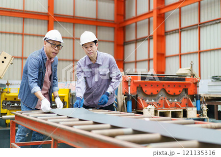 Industrial engineer team works together in factory. Asian specialist technicians or engineers are working in the metal sheet blending factory.  121135316