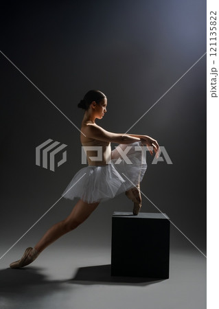 Ballerina performing an elegant pose on a stage with dramatic lighting 121135822