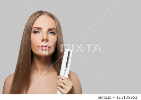 Glamorous woman with long hair using a straight hair iron and doing a hairstyle 121135952