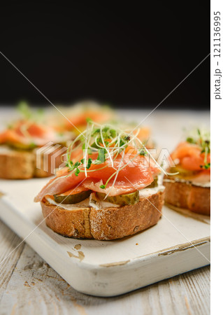 Delicious open-faced sandwiches with smoked salmon and fresh toppings on a wooden platter 121136995