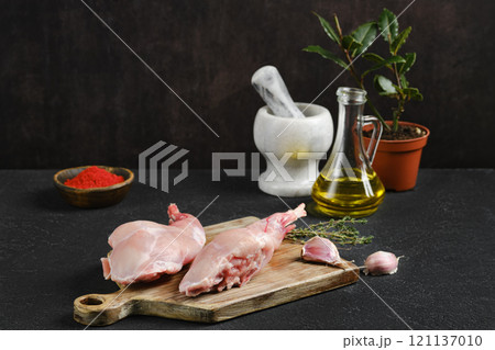 Fresh rabbit legs prepared for cooking with herbs and spices on a wooden cutting board Fresh rabbit legs prepared for cooking with herbs and spices on a wooden cutting board 121137010
