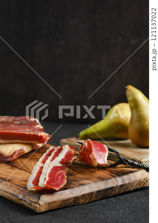 Sliced cured duck meat and fresh pears arranged on wooden cutting board in cozy kitchen setting 121137022