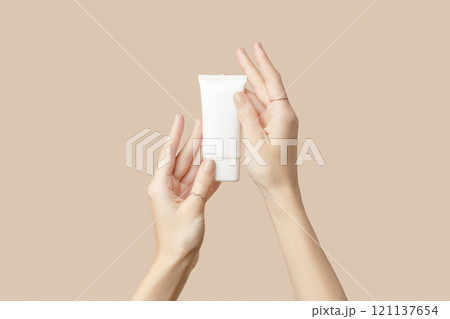 A womans hands holding a white cosmetic tube on a beige background. Beauty treatment concept A womans hands holding a white cosmetic tube on a beige background. Beauty treatment concept 121137654