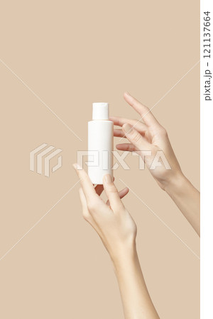 A womans hands holding a white cosmetic bottle on a beige background 121137664