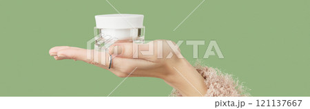 A womans hand in a sweater holds a jar of cream on a green background. Self care beauty treatment A womans hand in a sweater holds a jar of cream on a green background. Self care beauty treatment 121137667