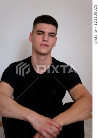 young casual man sitting with legs crossed and holding his head while smiling to the camera. isolated on white 121138025