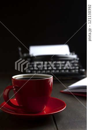 Red cup with coffee on table. Cup stands against background of an old typewriter. Concept of business breakfast. Morning of writer. 121138392