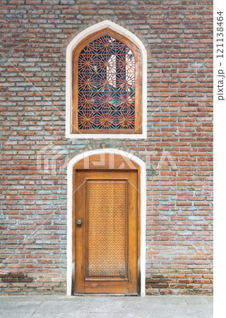 Intricate wooden door and patterned window on a rustic brick wall in an urban setting 121138464
