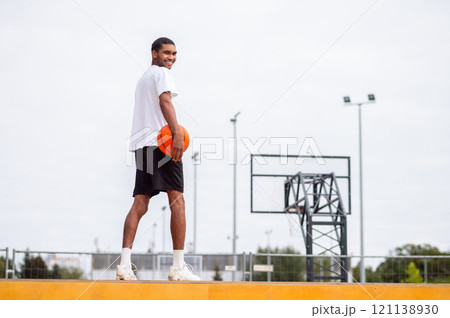 Tall man in sportswear standing with a ball in hands near the basketball playground 121138930