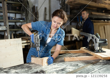 Work in woodworking enterprise - woman drills a hole with drill 121139258