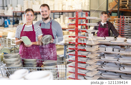 Positive artisans standing in pottery studio with ceramic pieces in hands 121139414