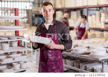 Enthusiastic ceramicist demonstrating handcrafted plates in ceramic studio 121139502