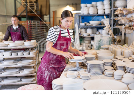 Female artisan cleaning plates with sponge in ceramics studio Female artisan cleaning plates with sponge in ceramics studio 121139504