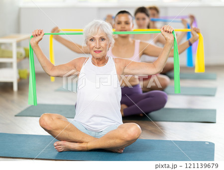 Senior lady performing exercises with resistance band in pilates class Senior lady performing exercises with resistance band in pilates class 121139679