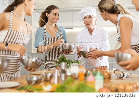 Elderly woman chef with bowl in hands tells women at culinary courses about traditions of cuisine Elderly woman chef with bowl in hands tells women at culinary courses about traditions of cuisine 121139838