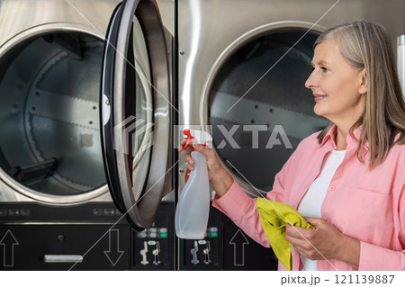 Mature caucasian woman cleaning the washing machine and looking involved Mature caucasian woman cleaning the washing machine and looking involved 121139887