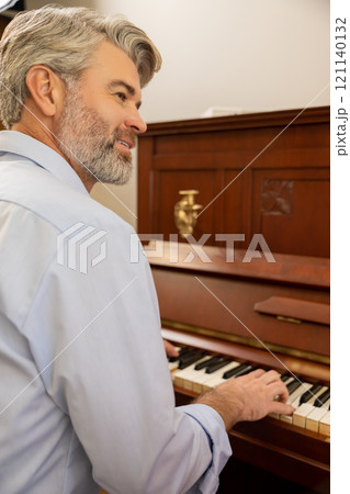 Gray-haired man playing the piano and looking aside 121140132