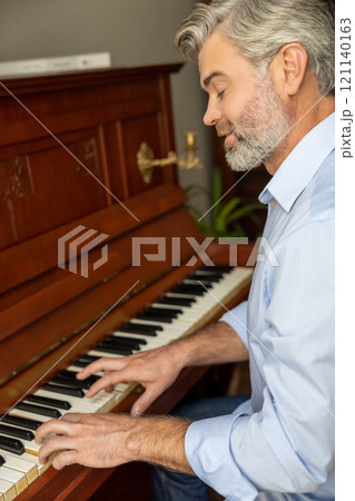 Gray-haired mature man playing the piano and looking involved 121140163
