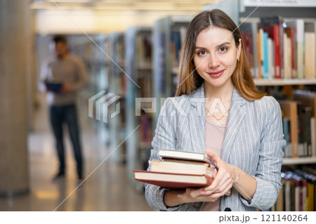 Adult woman with book standing near bookshelves in public library Adult woman with book standing near bookshelves in public library 121140264