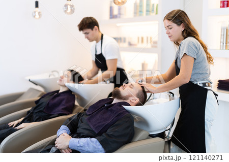 Young female hairdresser washing hair of male client 121140271