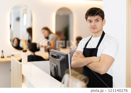 Male employee of barbershop stands near reception desk of salon, waits for visitors Male employee of barbershop stands near reception desk of salon, waits for visitors 121140276