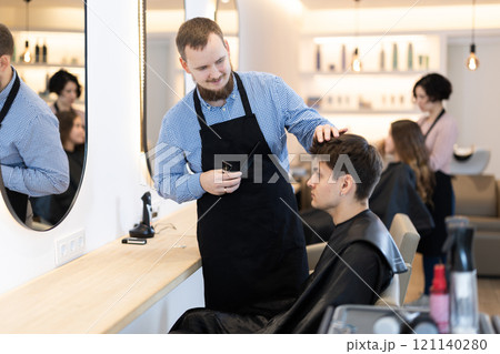 Young man barbershop employee stands next to male client, discussing details of haircut Young man barbershop employee stands next to male client, discussing details of haircut 121140280