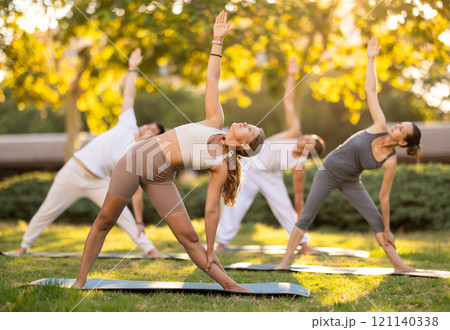 Girl leading outdoor group yoga class in summer park 121140338