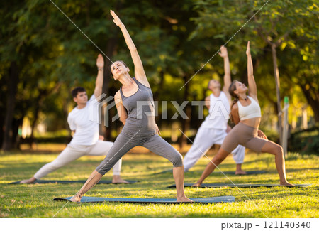 Yoga lesson visitors perform virabhadrasana in park 121140340