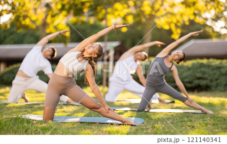Yoga lesson visitors with girl coach perform Parighasana in park 121140341