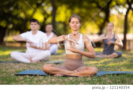 Girl meditating in lotus position during group yoga in park Girl meditating in lotus position during group yoga in park 121140354