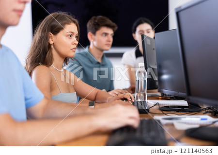 Girl student of computer courses looks at monitor screen, types on keyboard and does work 121140563
