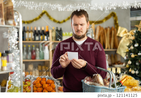 Young man shopping with list for Christmas snacks in store Young man shopping with list for Christmas snacks in store 121141125