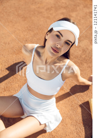 Pretty young tennis player in white clothes sitting on the tennis courts Pretty young tennis player in white clothes sitting on the tennis courts 121141741