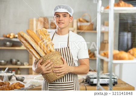 Young male baker holding baguettes in round wicker basket 121141848